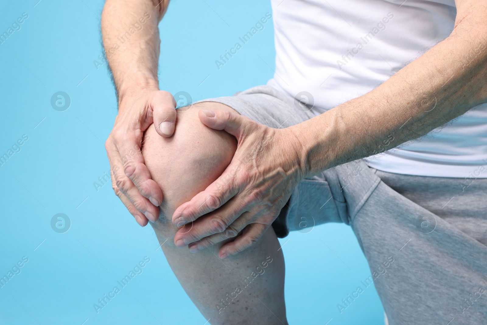 Photo of Senior man suffering from knee pain on light blue background, closeup