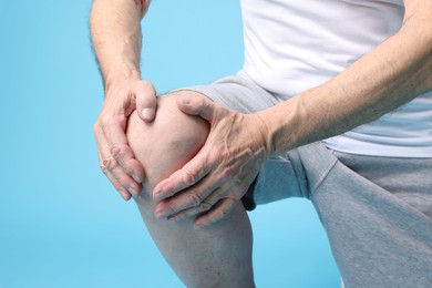 Photo of Senior man suffering from knee pain on light blue background, closeup