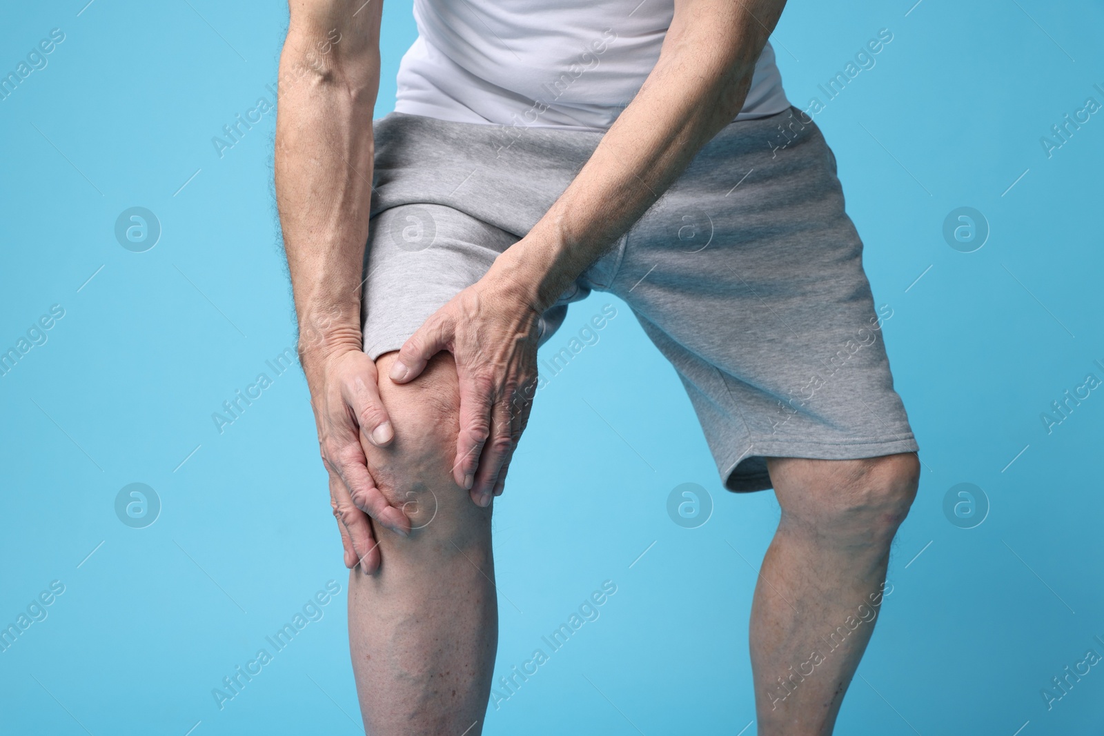 Photo of Senior man suffering from knee pain on light blue background, closeup