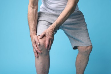 Photo of Senior man suffering from knee pain on light blue background, closeup