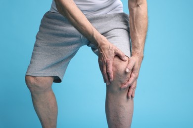 Photo of Senior man suffering from knee pain on light blue background, closeup