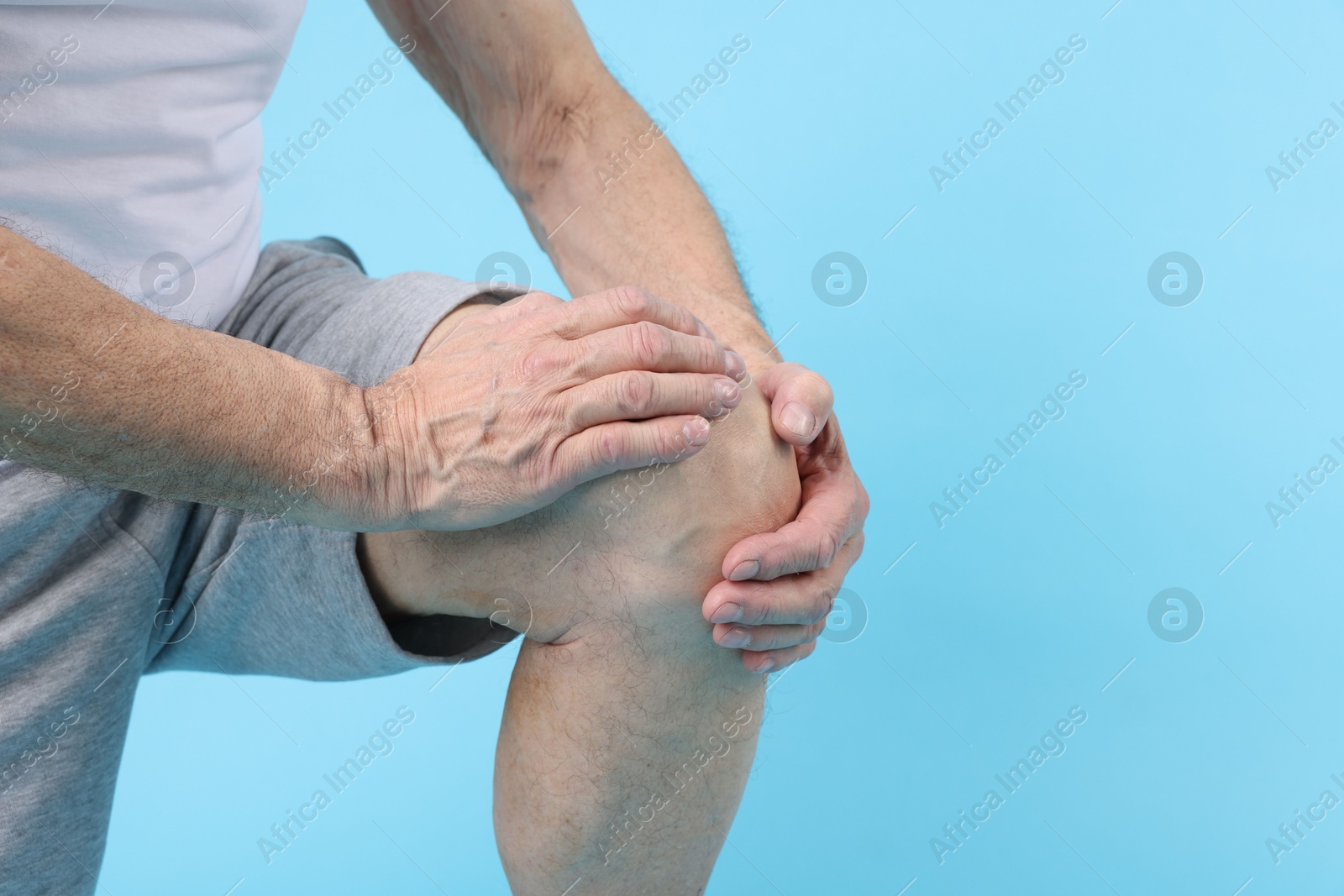 Photo of Senior man suffering from knee pain on light blue background, closeup. Space for text