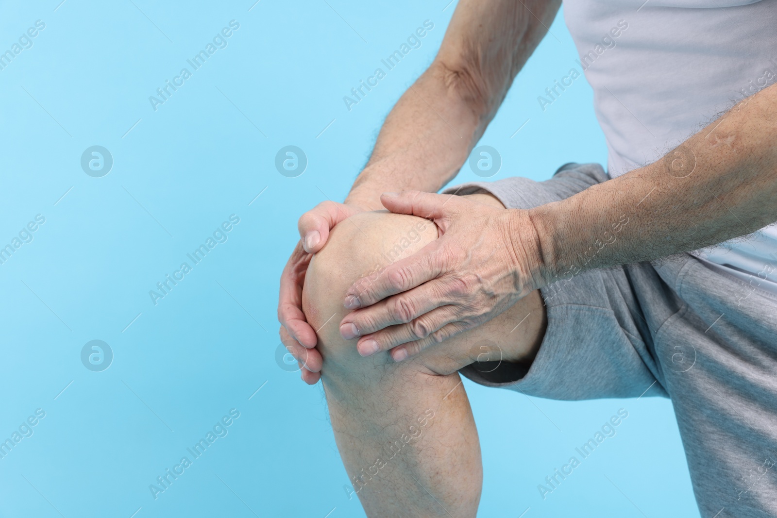 Photo of Senior man suffering from knee pain on light blue background, closeup. Space for text