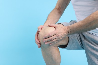 Photo of Senior man suffering from knee pain on light blue background, closeup. Space for text