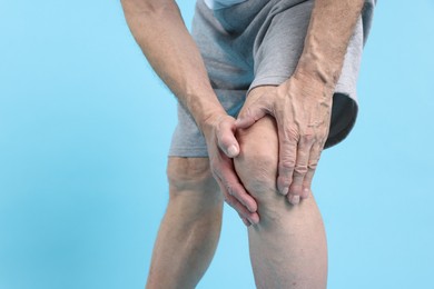 Photo of Senior man suffering from knee pain on light blue background, closeup