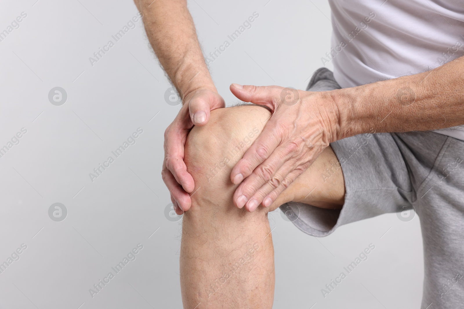 Photo of Senior man suffering from knee pain on light grey background, closeup