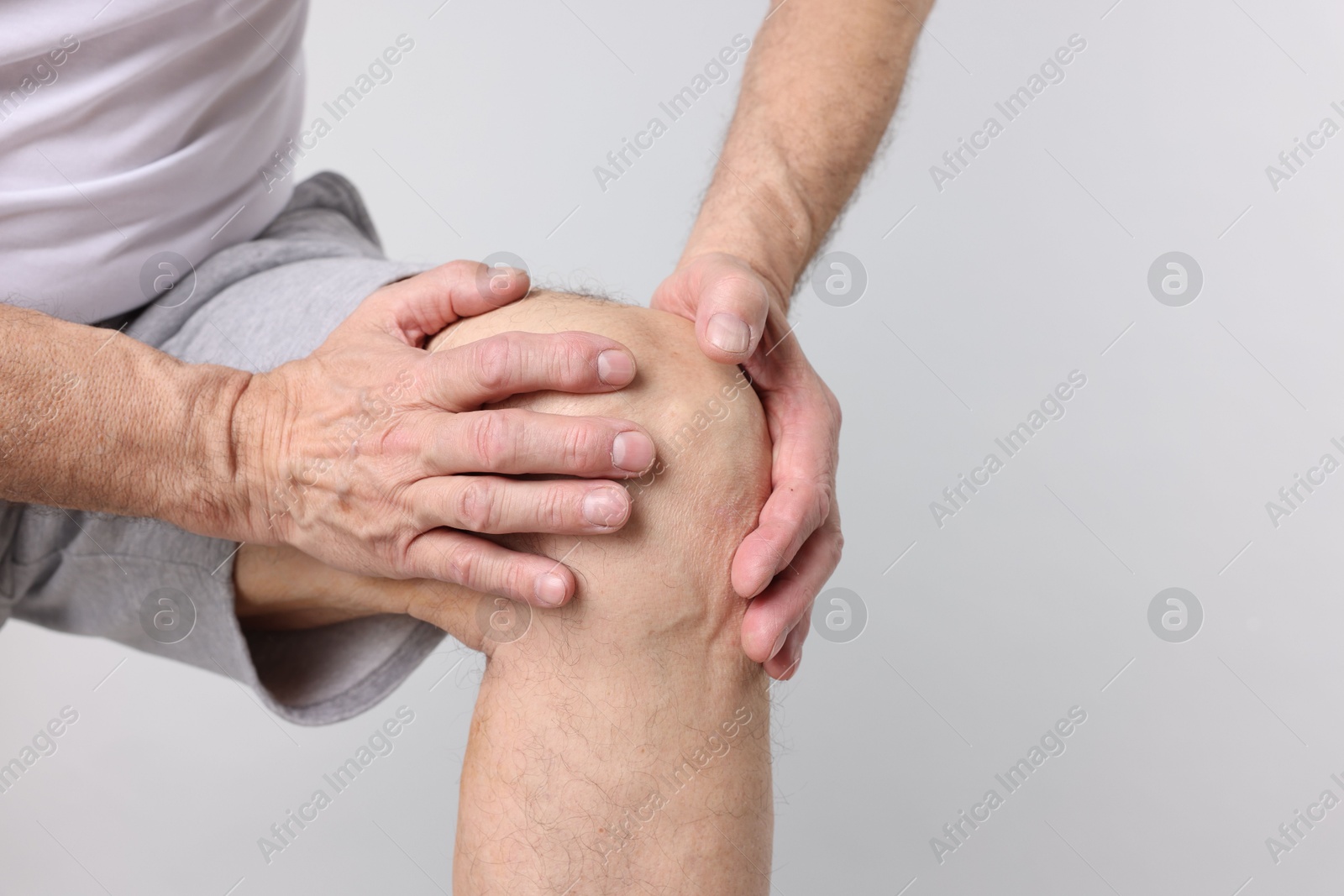 Photo of Senior man suffering from knee pain on light grey background, closeup