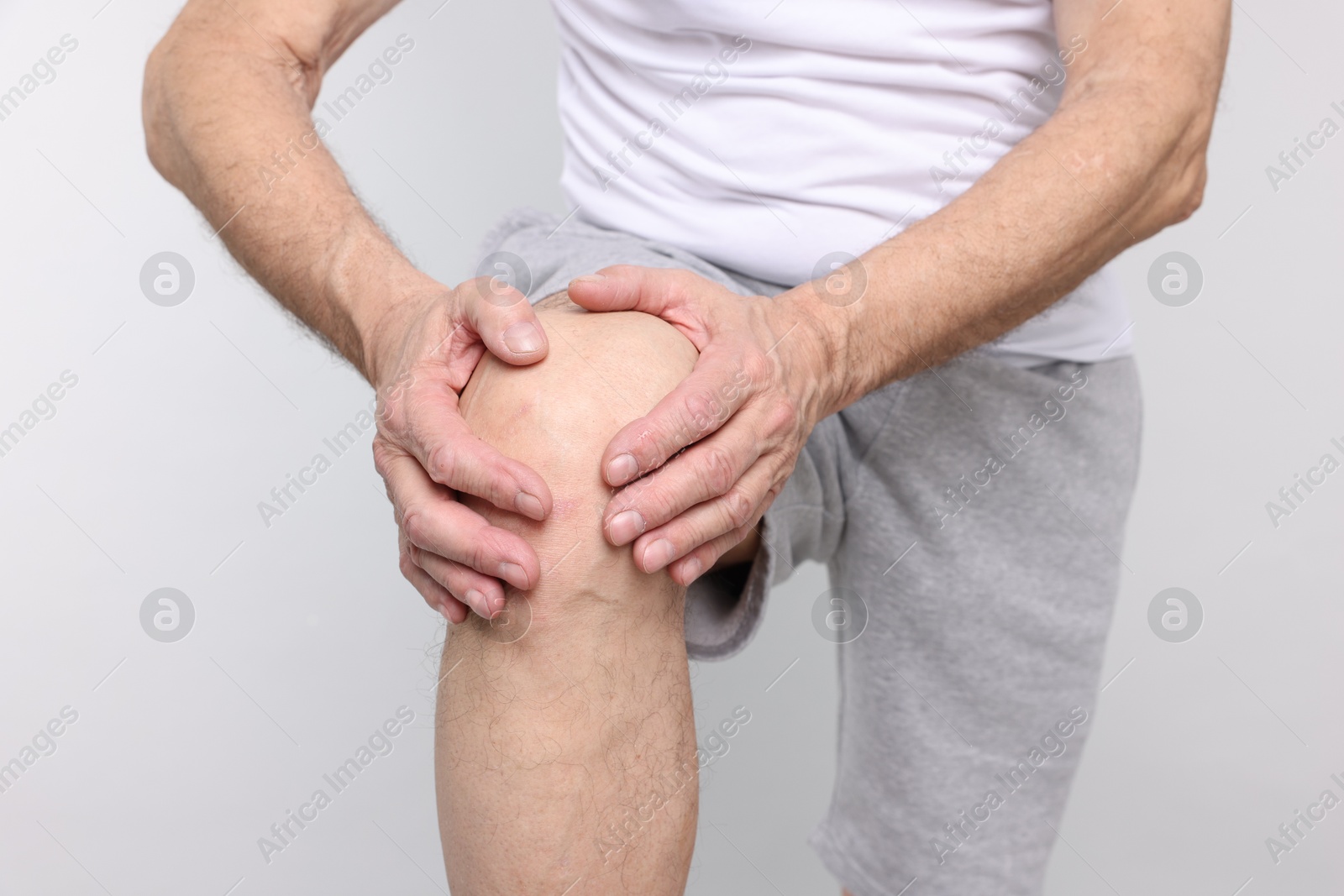 Photo of Senior man suffering from knee pain on light grey background, closeup