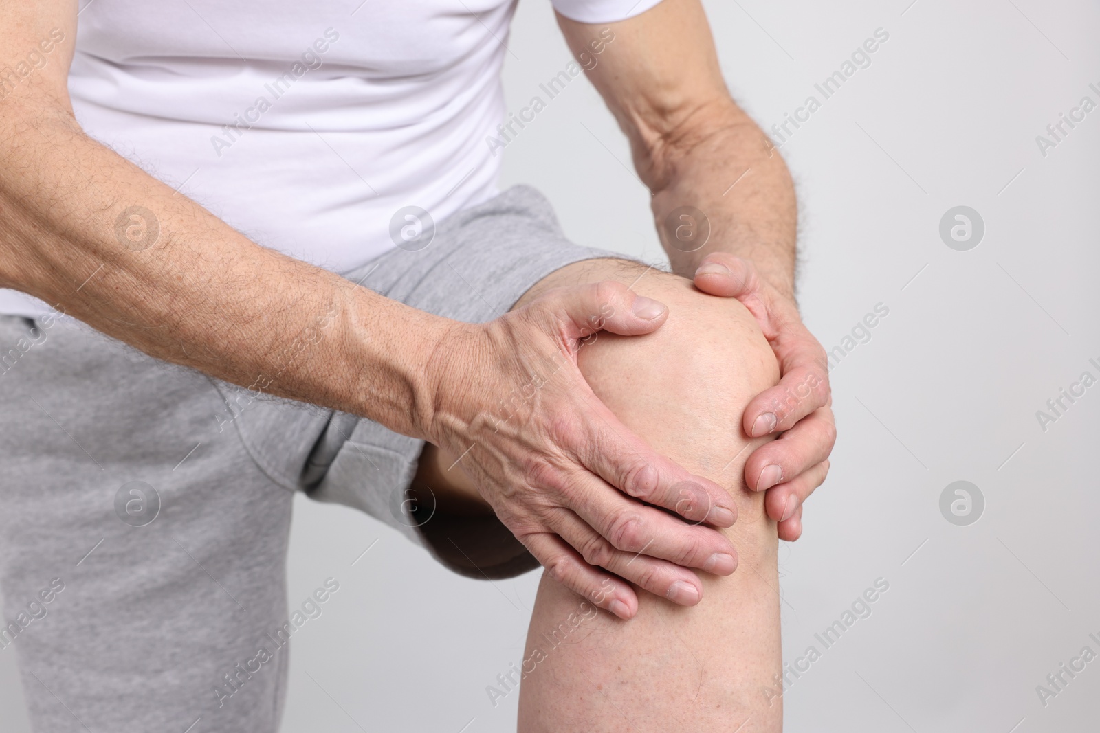 Photo of Senior man suffering from knee pain on light grey background, closeup