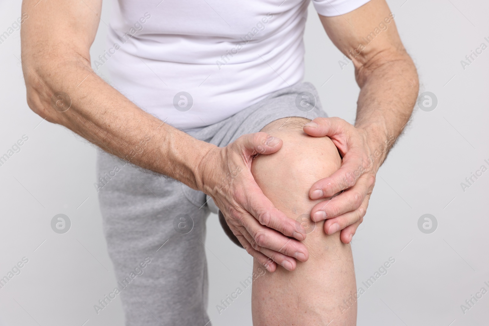 Photo of Senior man suffering from knee pain on light grey background, closeup