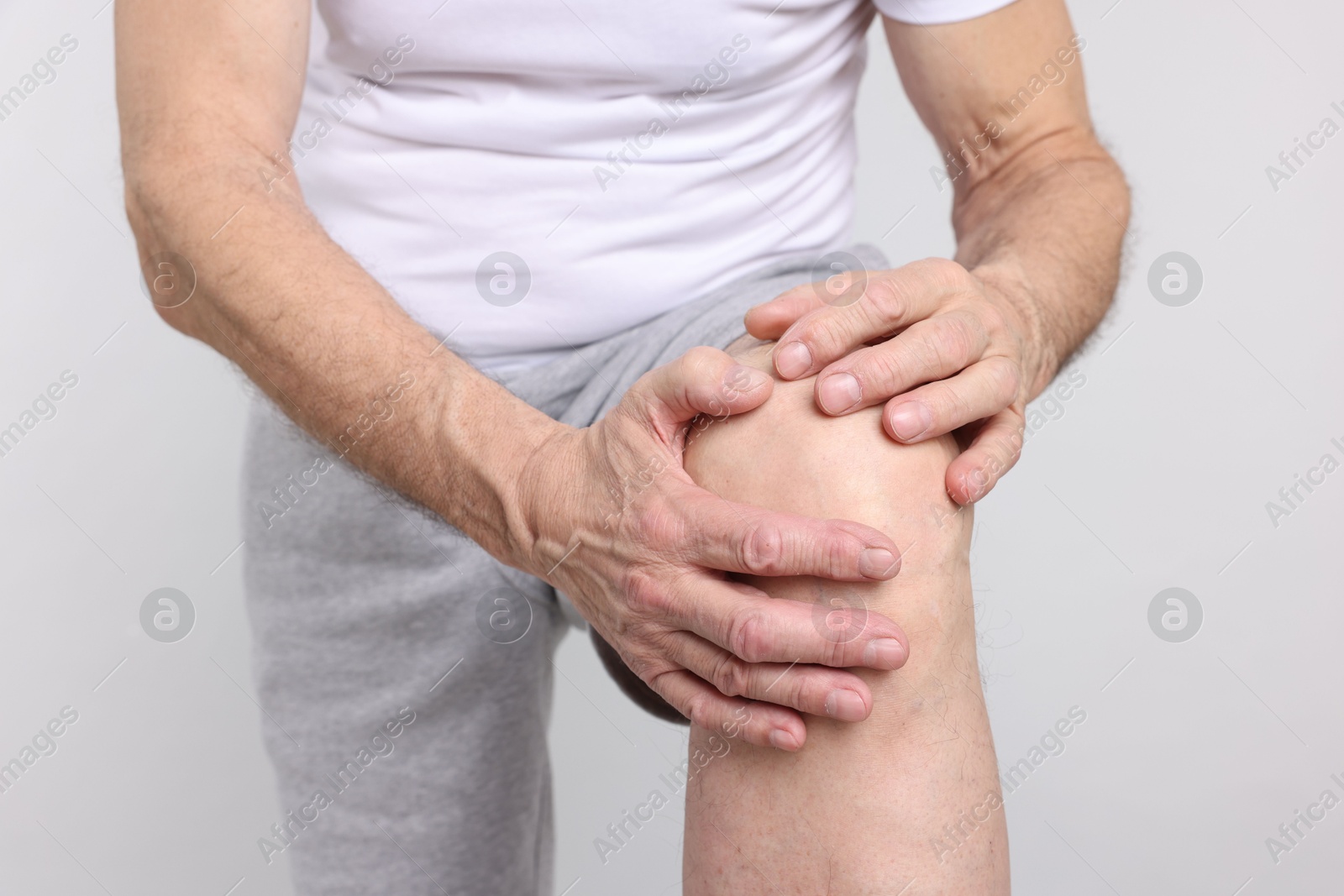 Photo of Senior man suffering from knee pain on light grey background, closeup