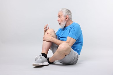 Photo of Senior man suffering from knee pain on light grey background