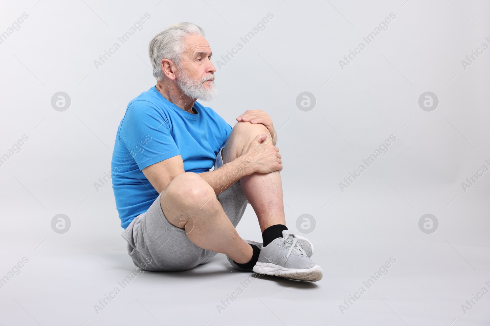 Photo of Senior man suffering from knee pain on light grey background. Space for text