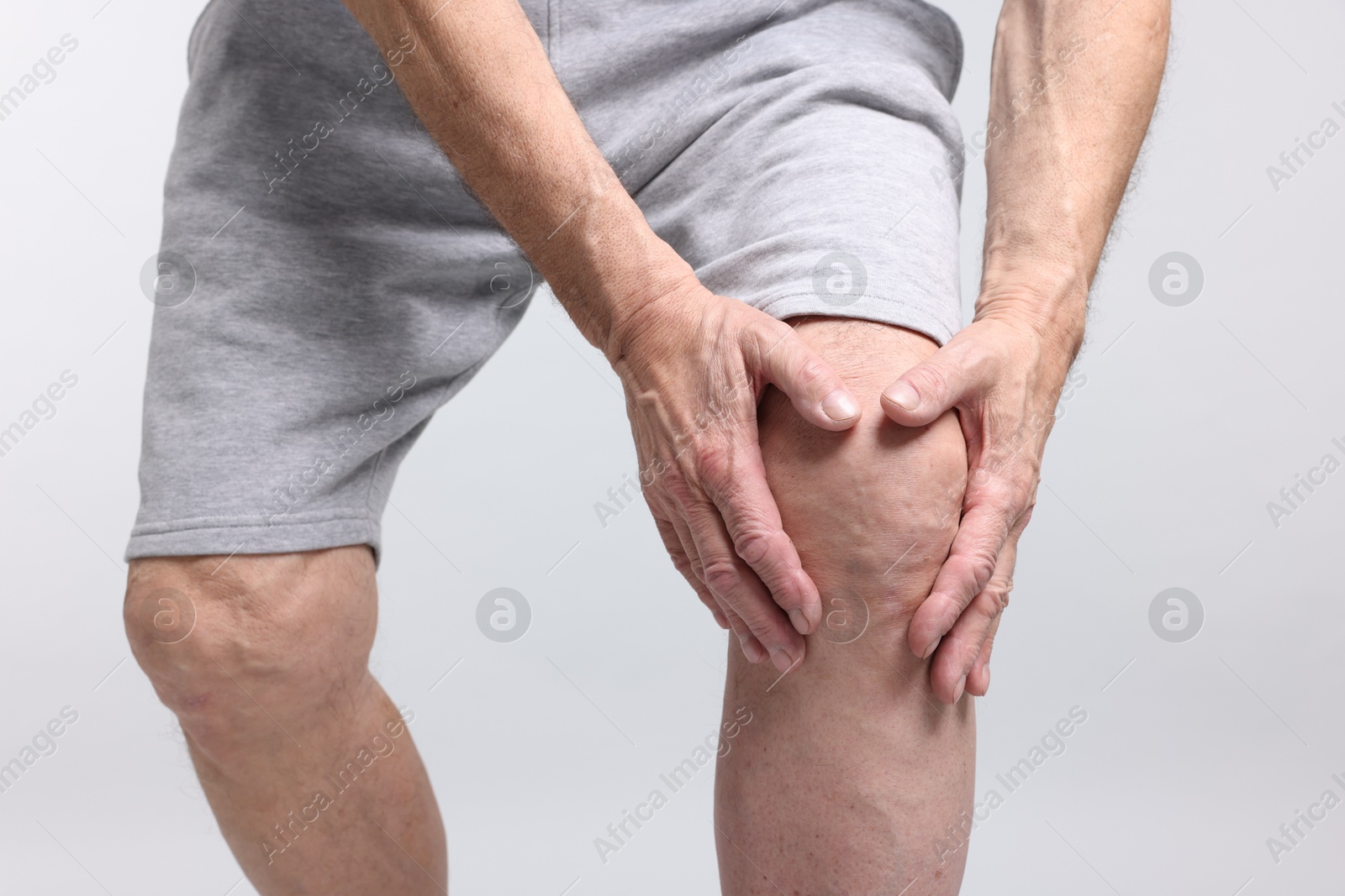 Photo of Senior man suffering from knee pain on light grey background, closeup