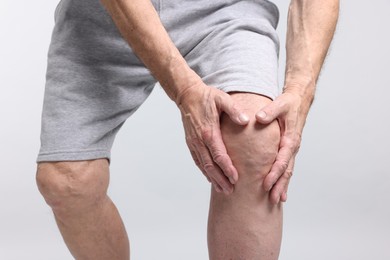 Photo of Senior man suffering from knee pain on light grey background, closeup