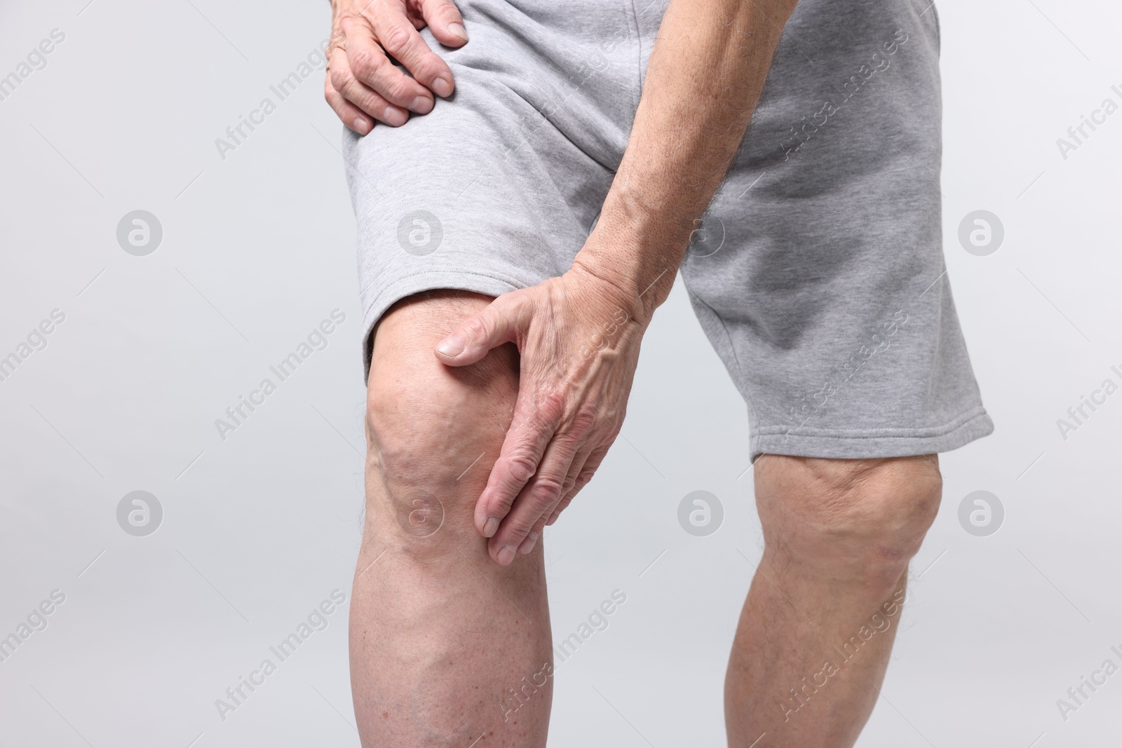 Photo of Senior man suffering from knee pain on light grey background, closeup