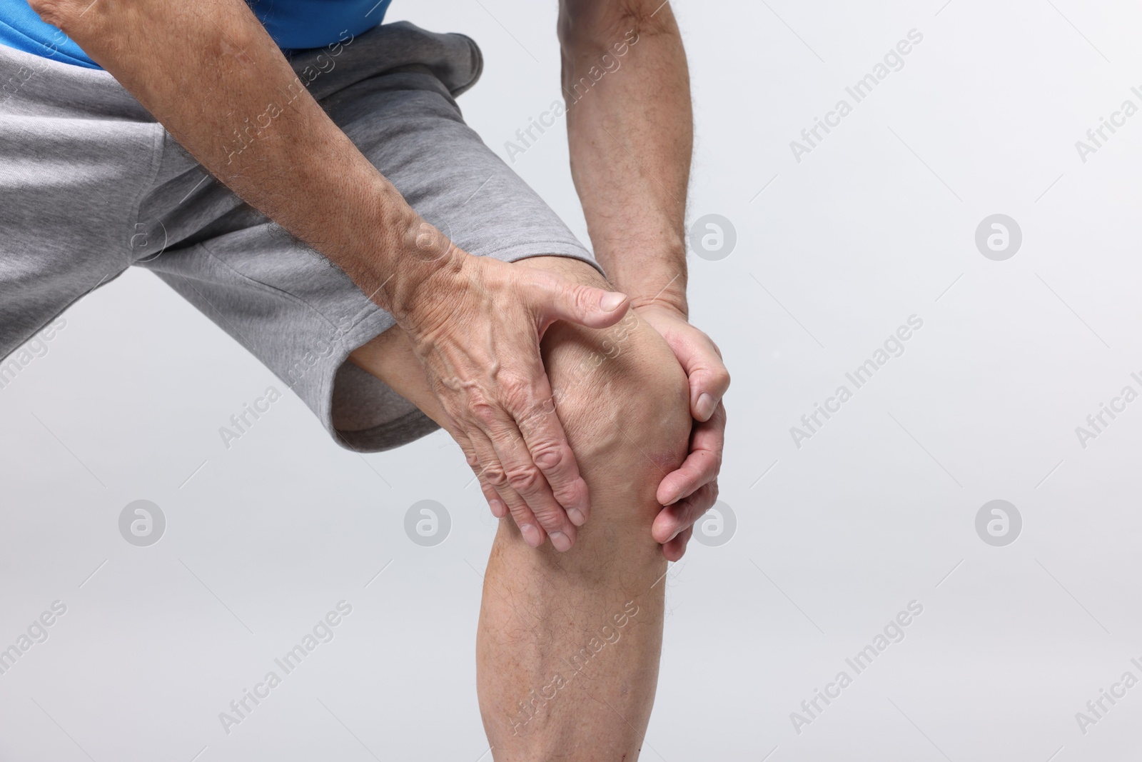 Photo of Senior man suffering from knee pain on light grey background, closeup. Space for text