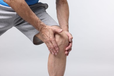 Photo of Senior man suffering from knee pain on light grey background, closeup. Space for text