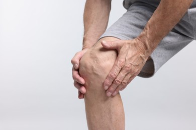 Photo of Senior man suffering from knee pain on light grey background, closeup