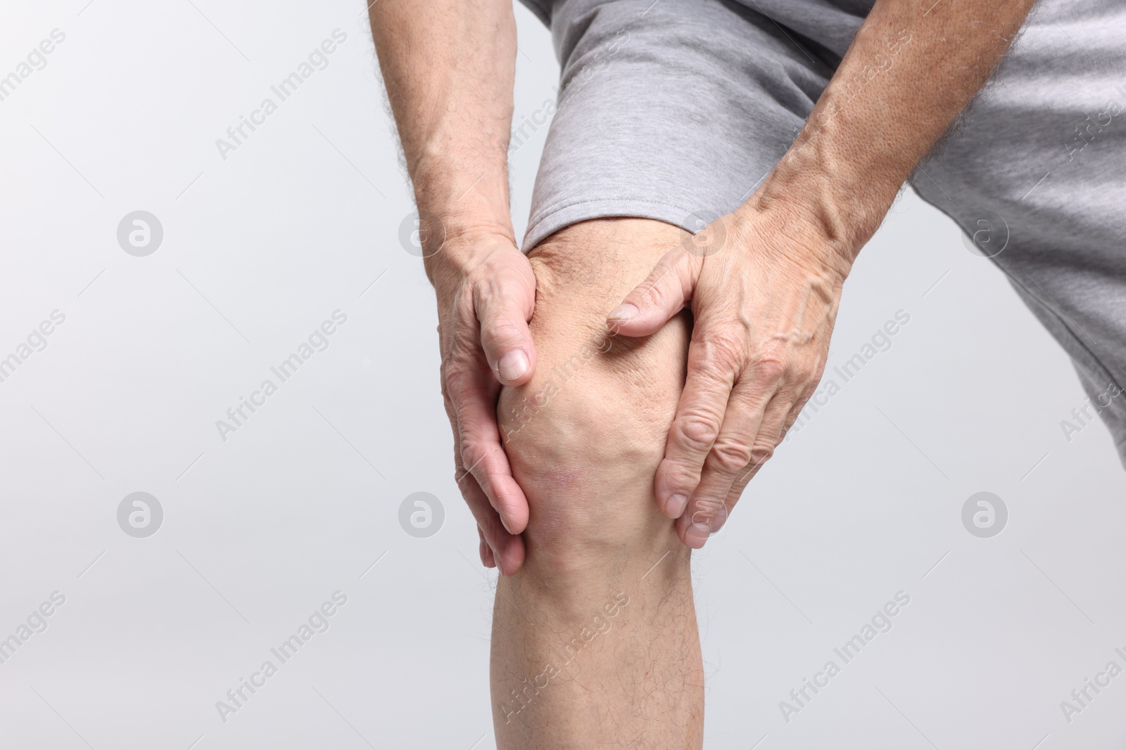 Photo of Senior man suffering from knee pain on light grey background, closeup