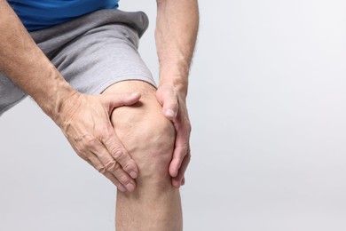 Photo of Senior man suffering from knee pain on light grey background, closeup. Space for text