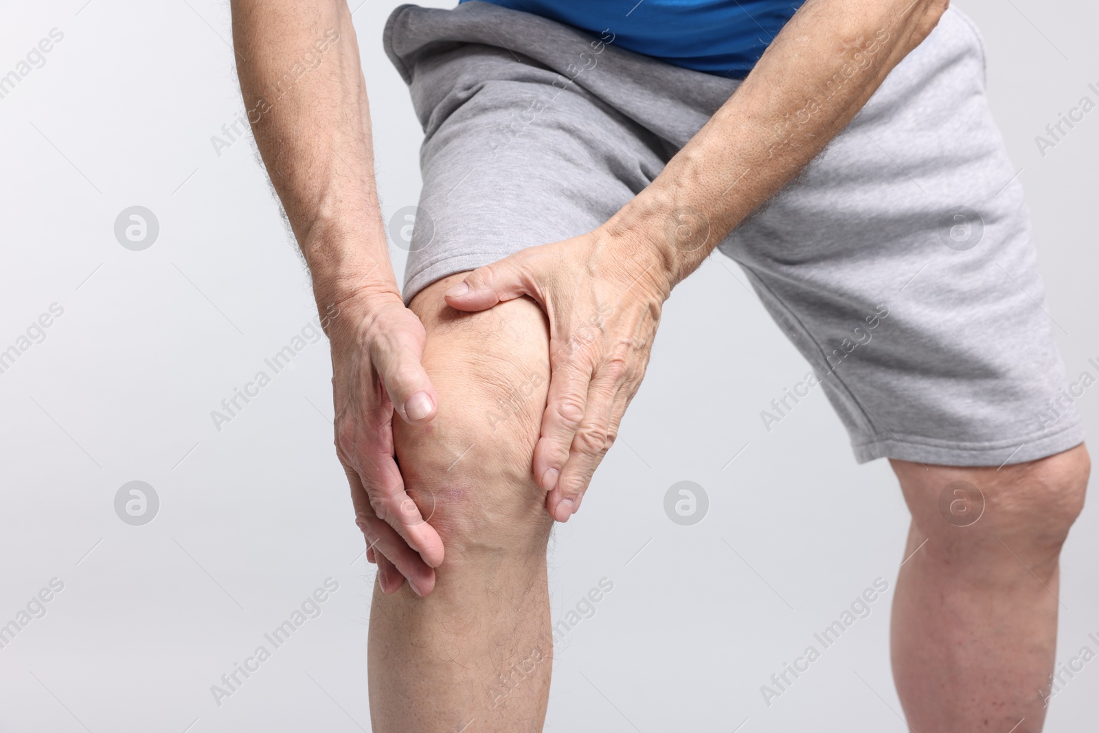 Photo of Senior man suffering from knee pain on light grey background, closeup