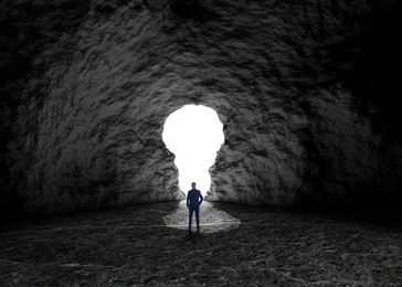 Image of Businessman looking at hole in shape of light bulb in dark cave. Idea, successful strategy