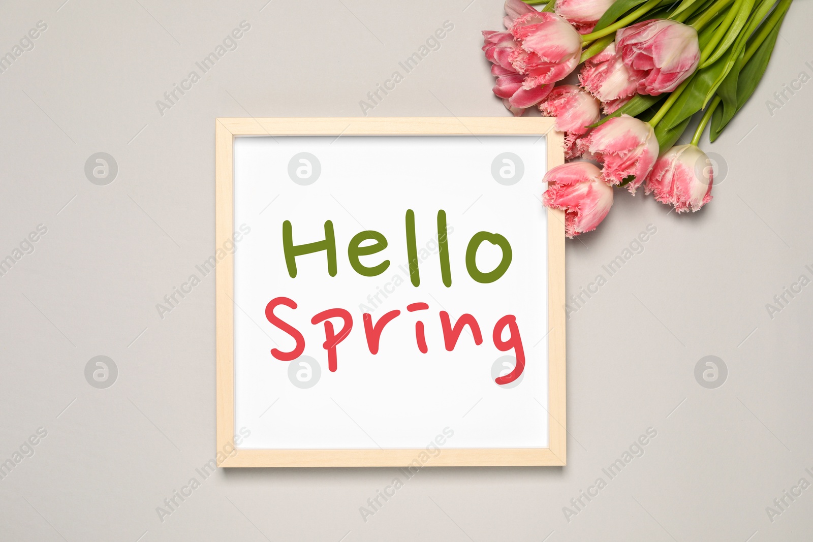 Image of Hello Spring card in frame and beautiful tulips on light grey background, flat lay