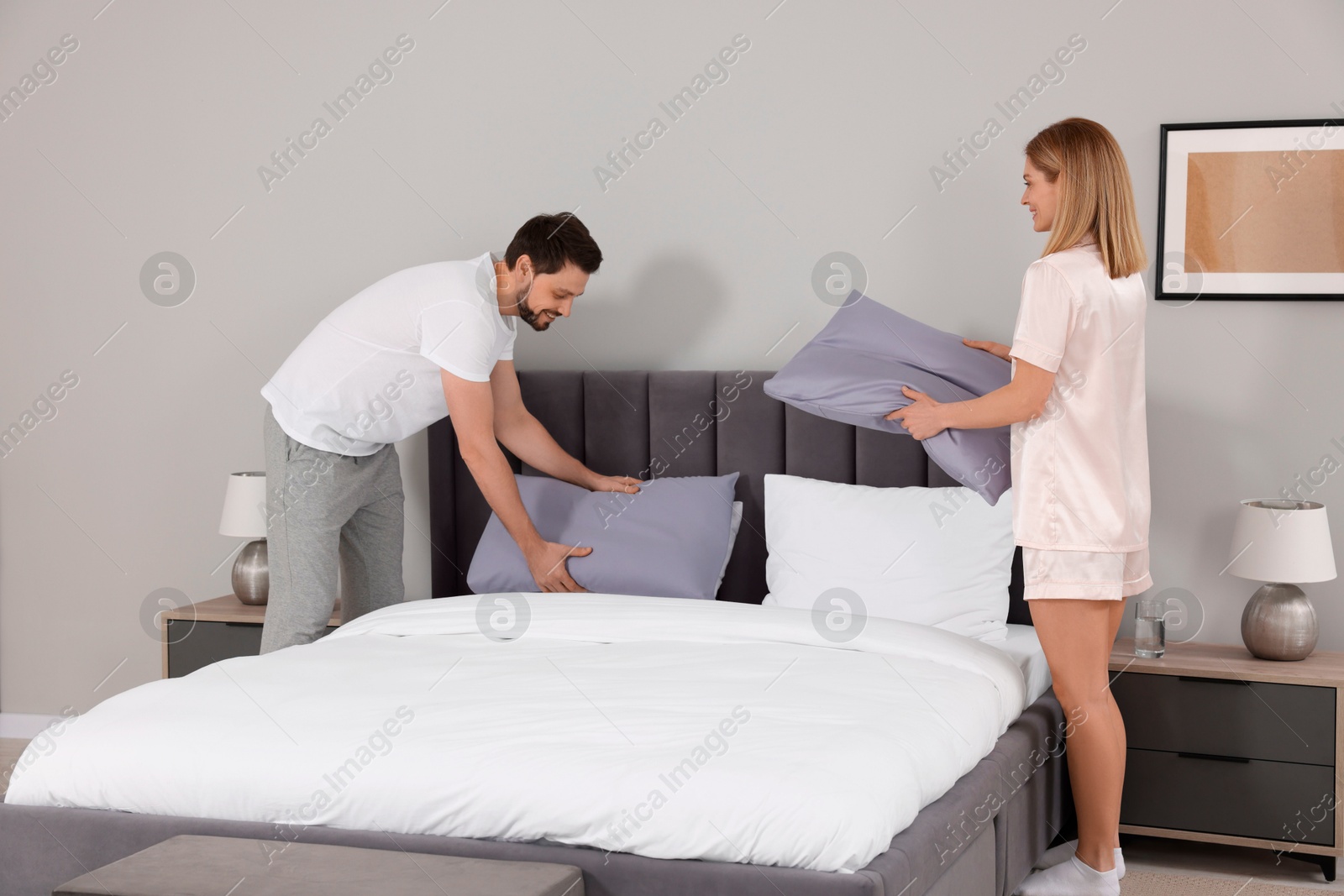 Photo of Couple changing bed linens in room. Domestic chores