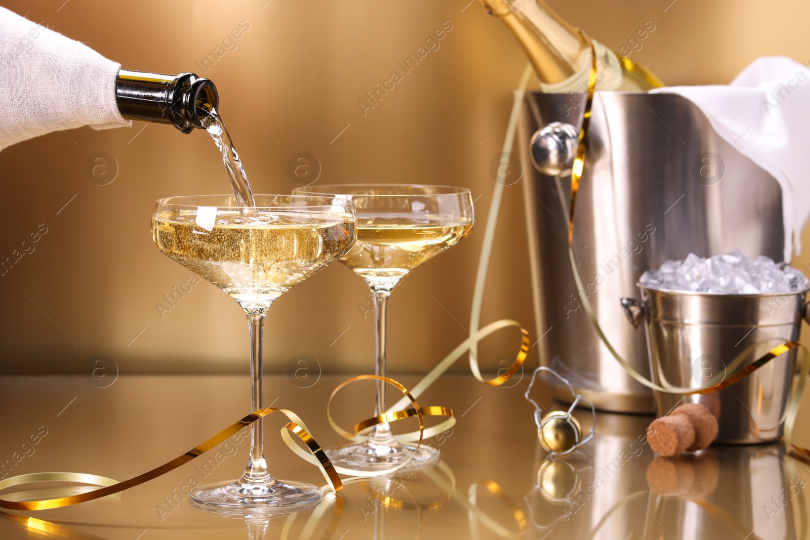 Photo of Pouring champagne into glass against golden background, closeup