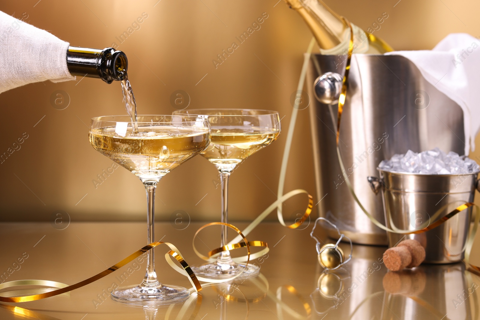 Photo of Pouring champagne into glass against golden background, closeup