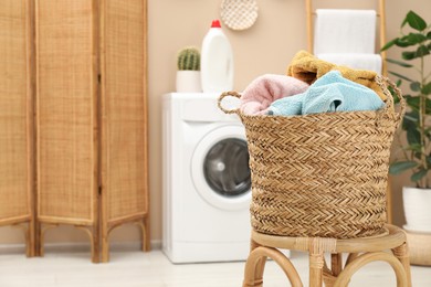 Photo of Wicker basket full of laundry on chair in bathroom