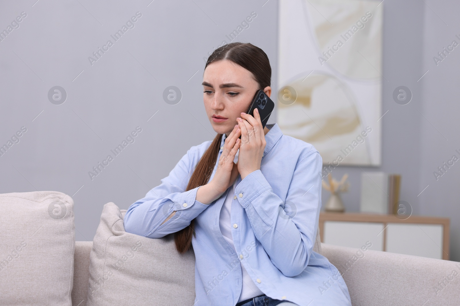 Photo of Depressed woman calling hotline for mental health help on sofa at home