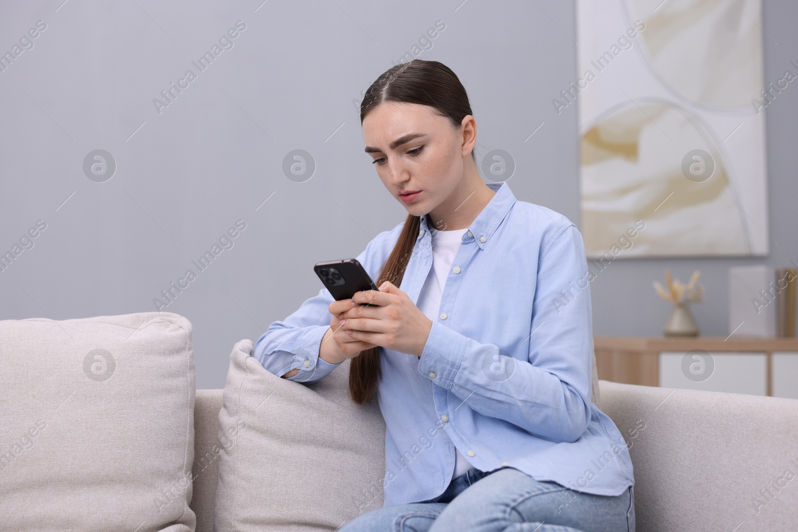 Photo of Depressed woman calling hotline for mental health help on sofa at home