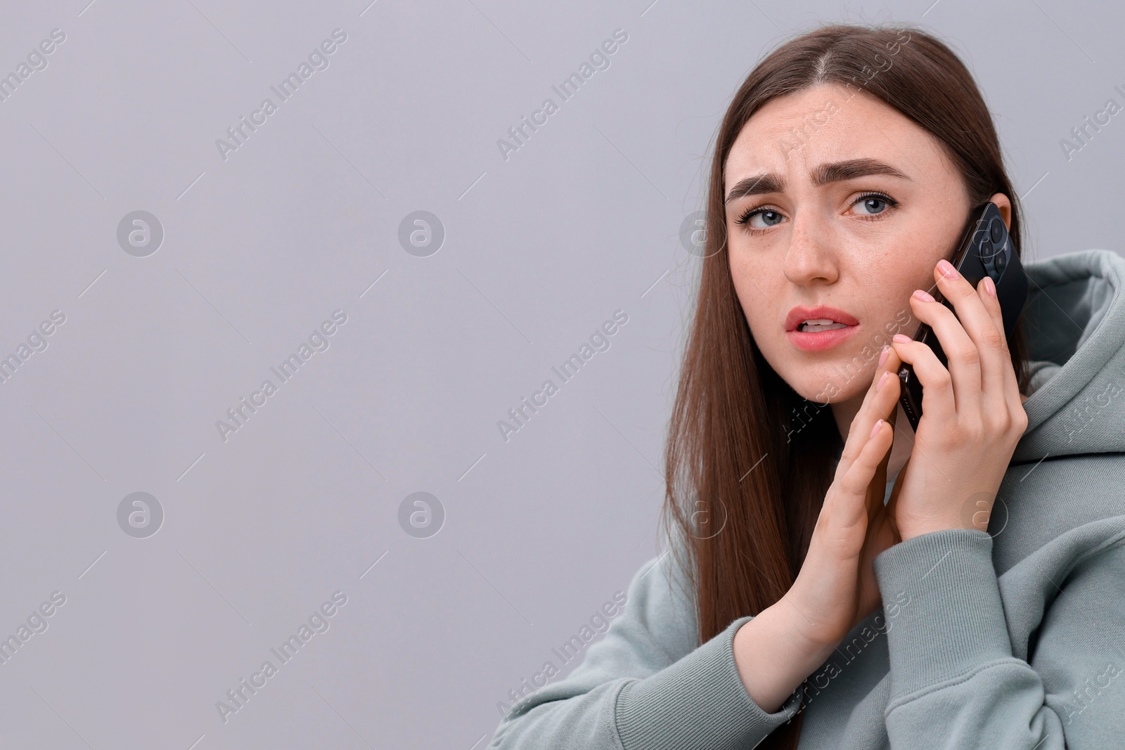 Photo of Stressed woman calling hotline for mental health help on grey background. Space for text