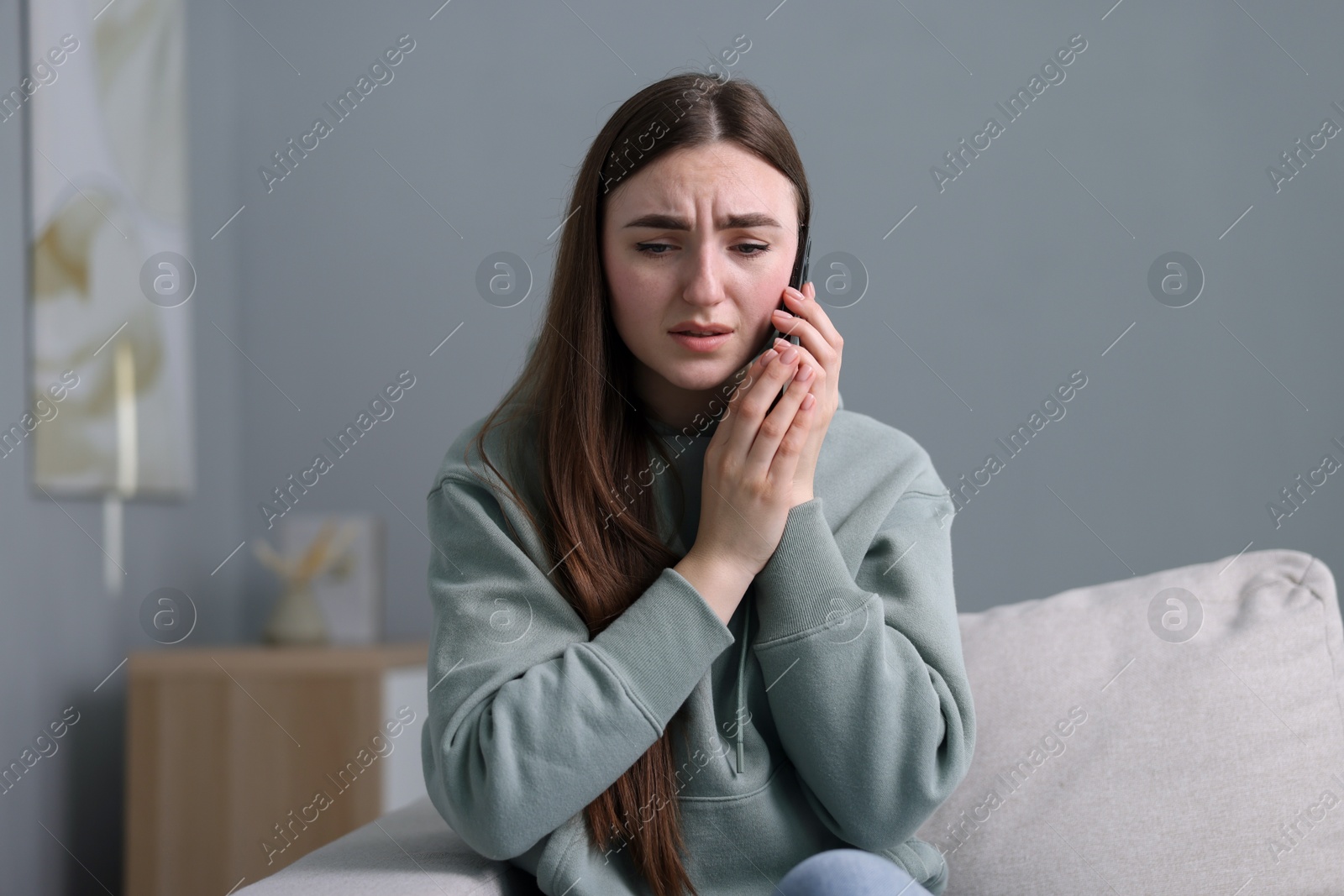 Photo of Depressed woman calling hotline for mental health help on sofa at home