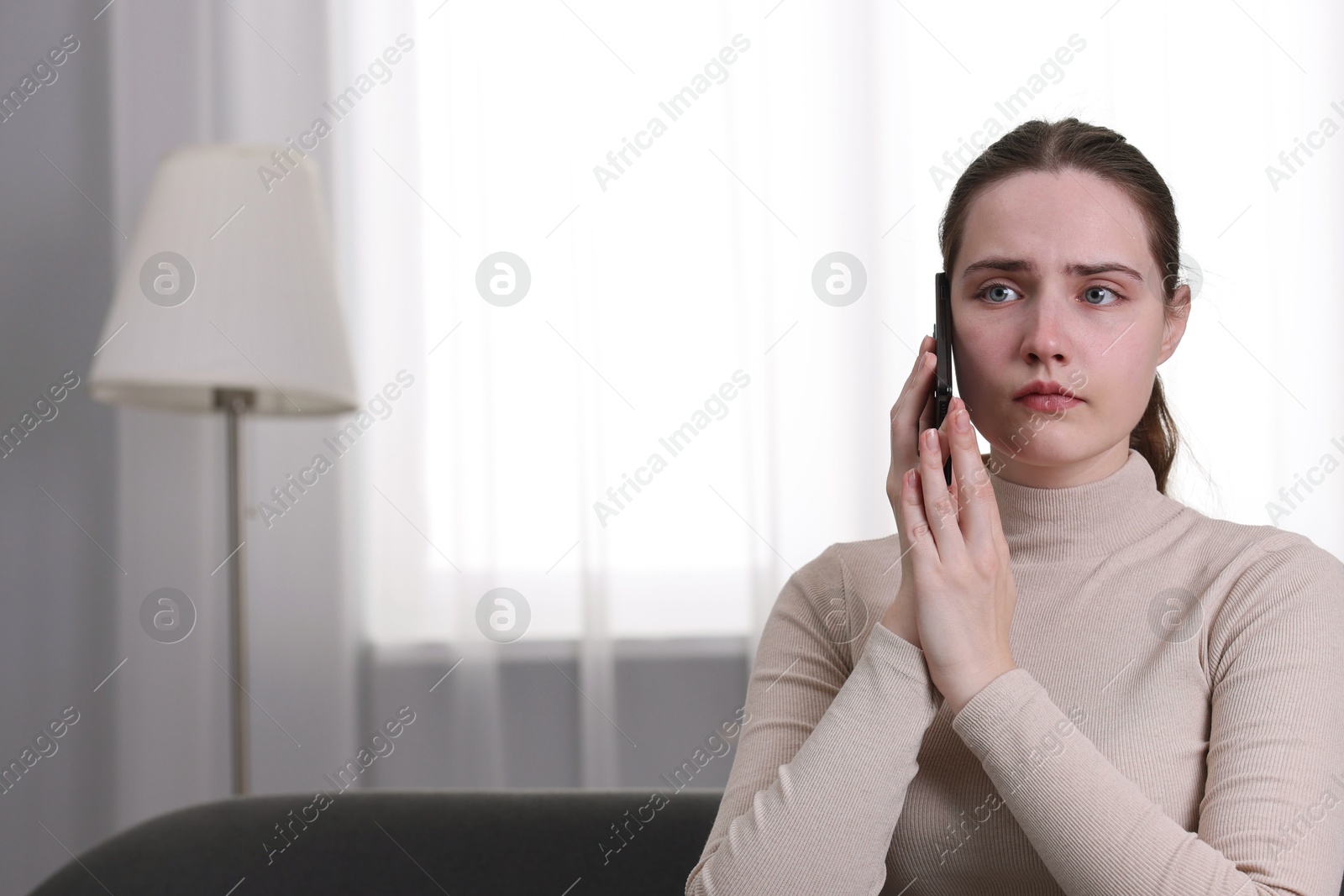 Photo of Depressed woman calling hotline for mental health help on sofa at home. Space for text