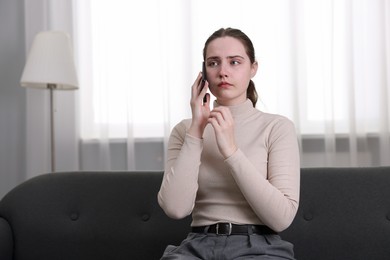 Photo of Depressed woman calling hotline for mental health help on sofa at home