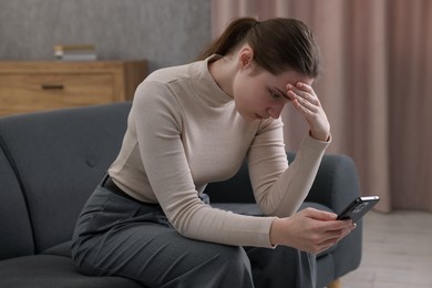 Photo of Depressed woman calling hotline for mental health help on sofa at home