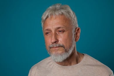 Photo of Sad senior man crying on blue background, closeup