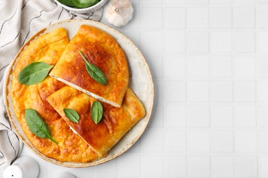 Photo of Tasty calzones with basil and cheese on white tiled table, top view. Space for text