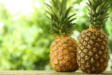 Photo of Fresh ripe pineapples on wooden table against blurred background, space for text