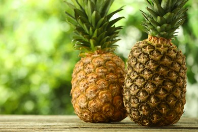 Photo of Fresh ripe pineapples on wooden table against blurred background, space for text