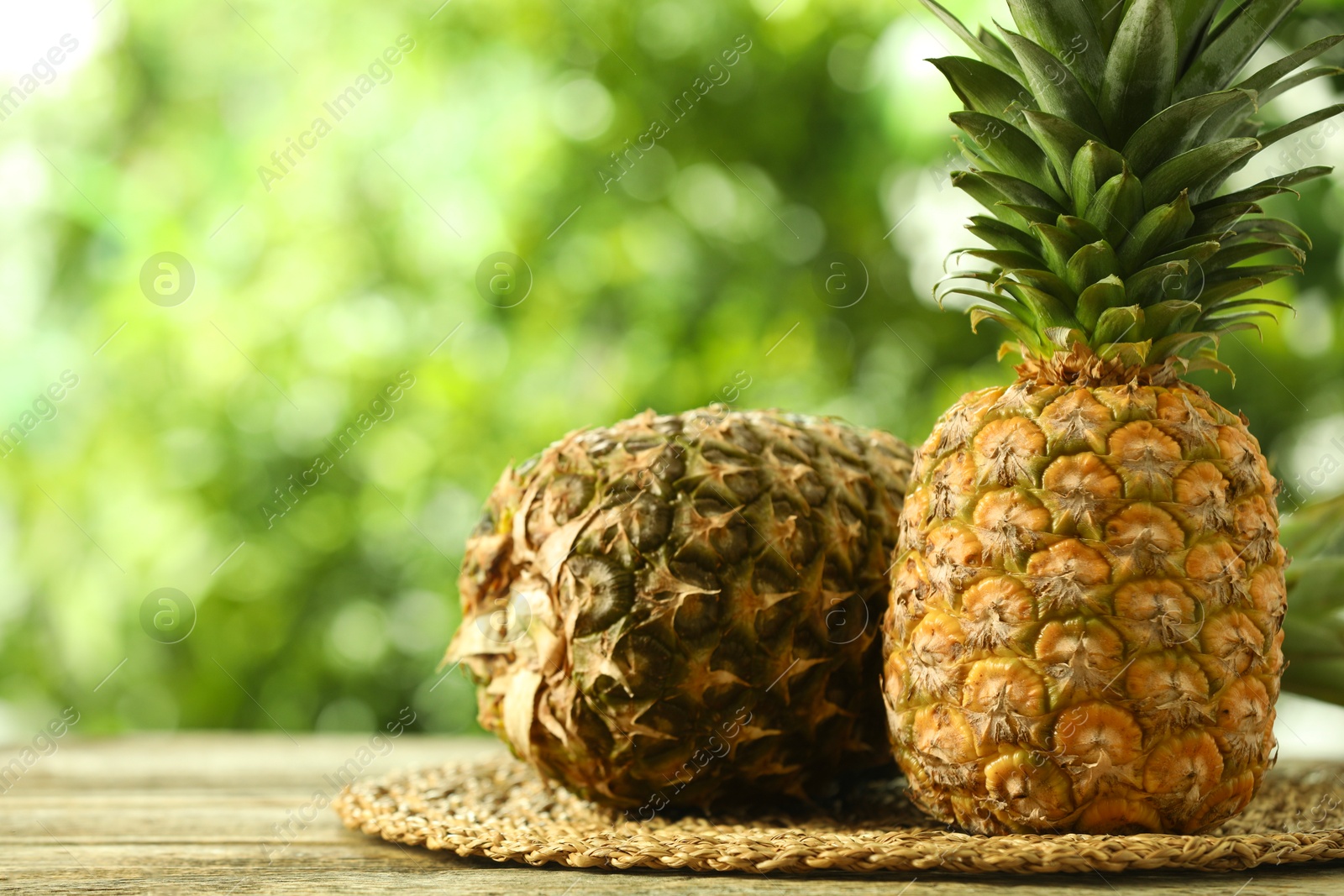 Photo of Fresh ripe pineapples on wooden table against blurred background, space for text