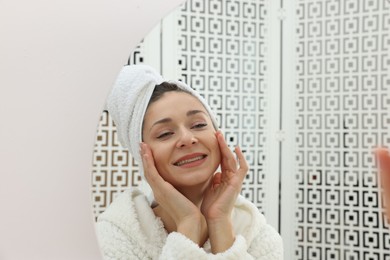 Photo of Spa day. Beautiful woman in bathrobe near mirror indoors