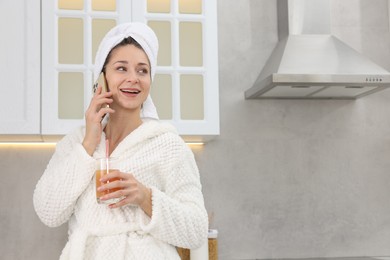 Photo of Beautiful woman with glass of juice talking on smartphone after spa procedure in kitchen, space for text