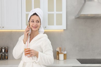 Photo of Beautiful woman with glass of juice talking on smartphone after spa procedure in kitchen, space for text