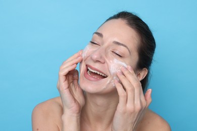 Photo of Spa day. Happy woman applying mask onto her face on light blue background