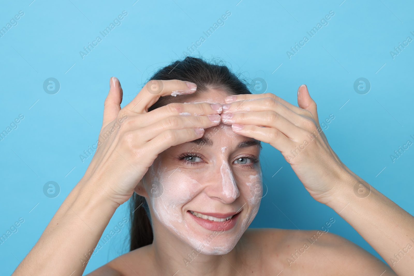 Photo of Spa day. Happy woman applying mask onto her face on light blue background