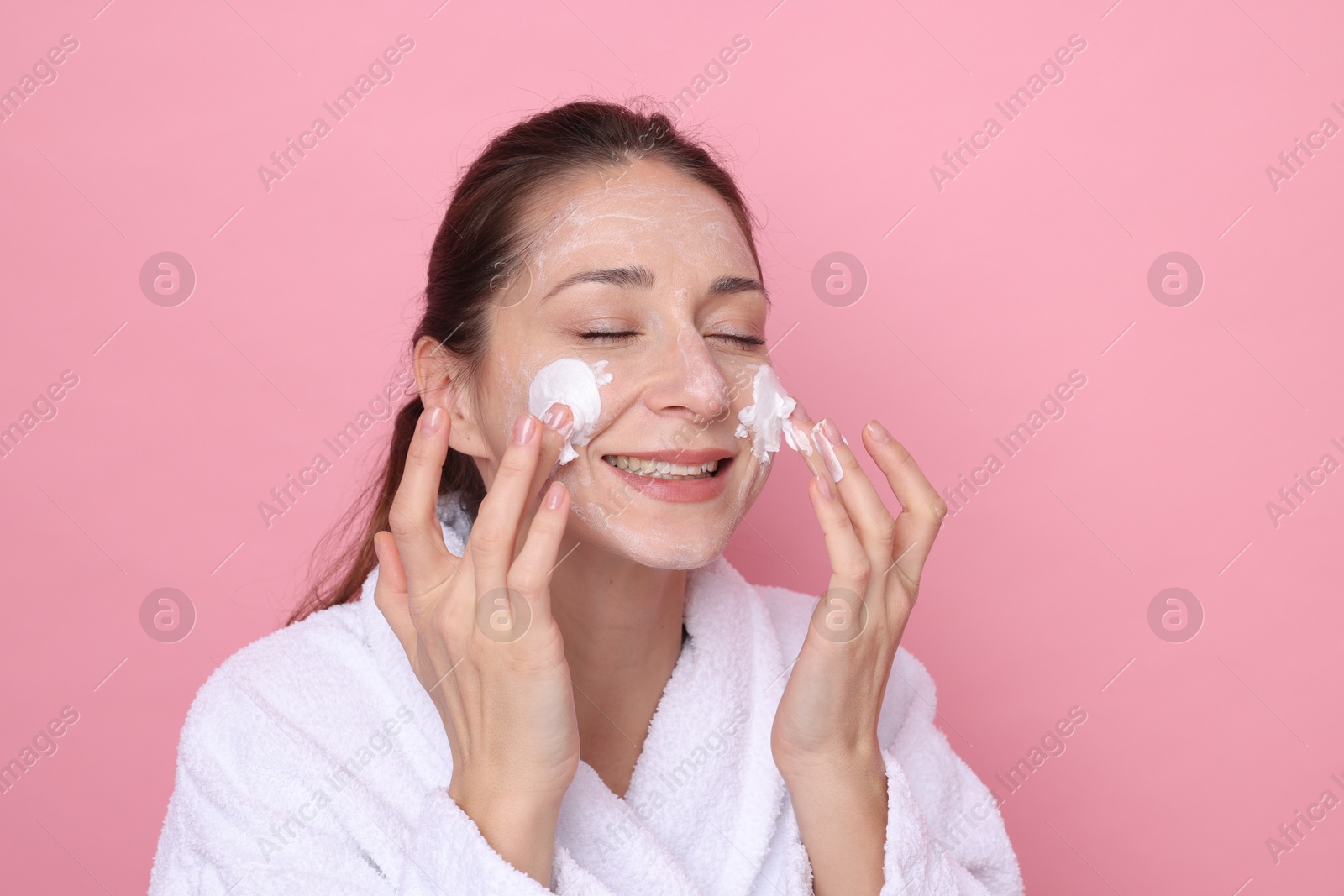 Photo of Spa day. Beautiful woman applying mask onto her face on pink background